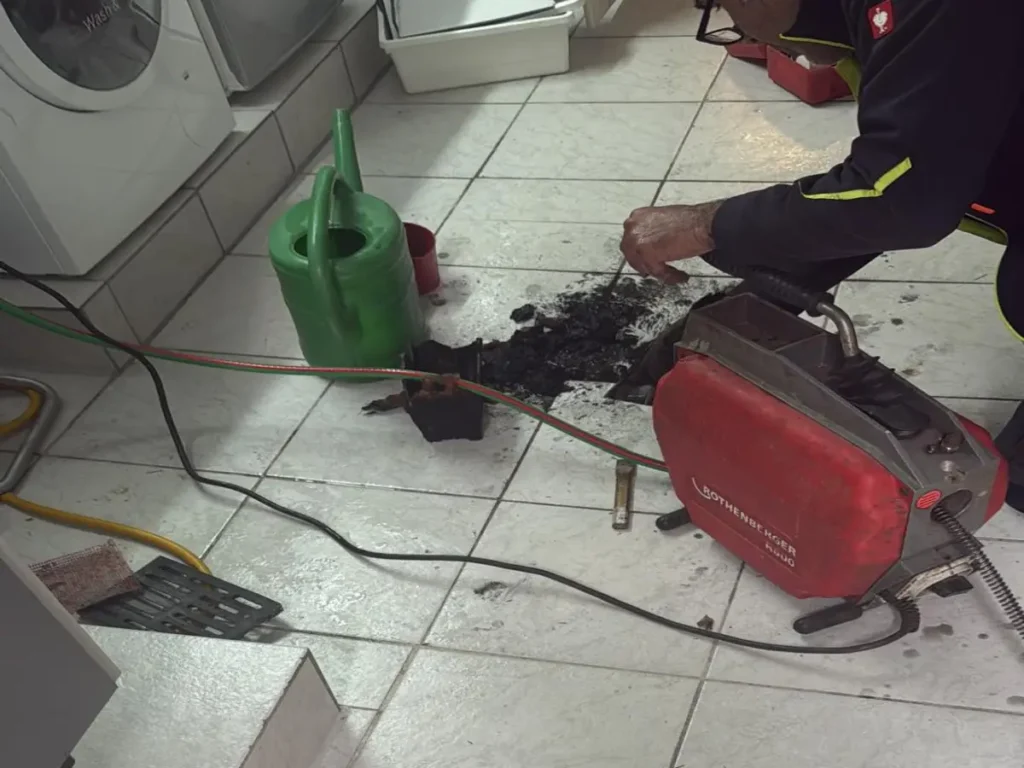 Der Rohrreiniger arbeitet mit einer Rothenberger-Maschine an einem verstopften Abfluss im Hauswirtschaftsraum Rohrreinigung Essen